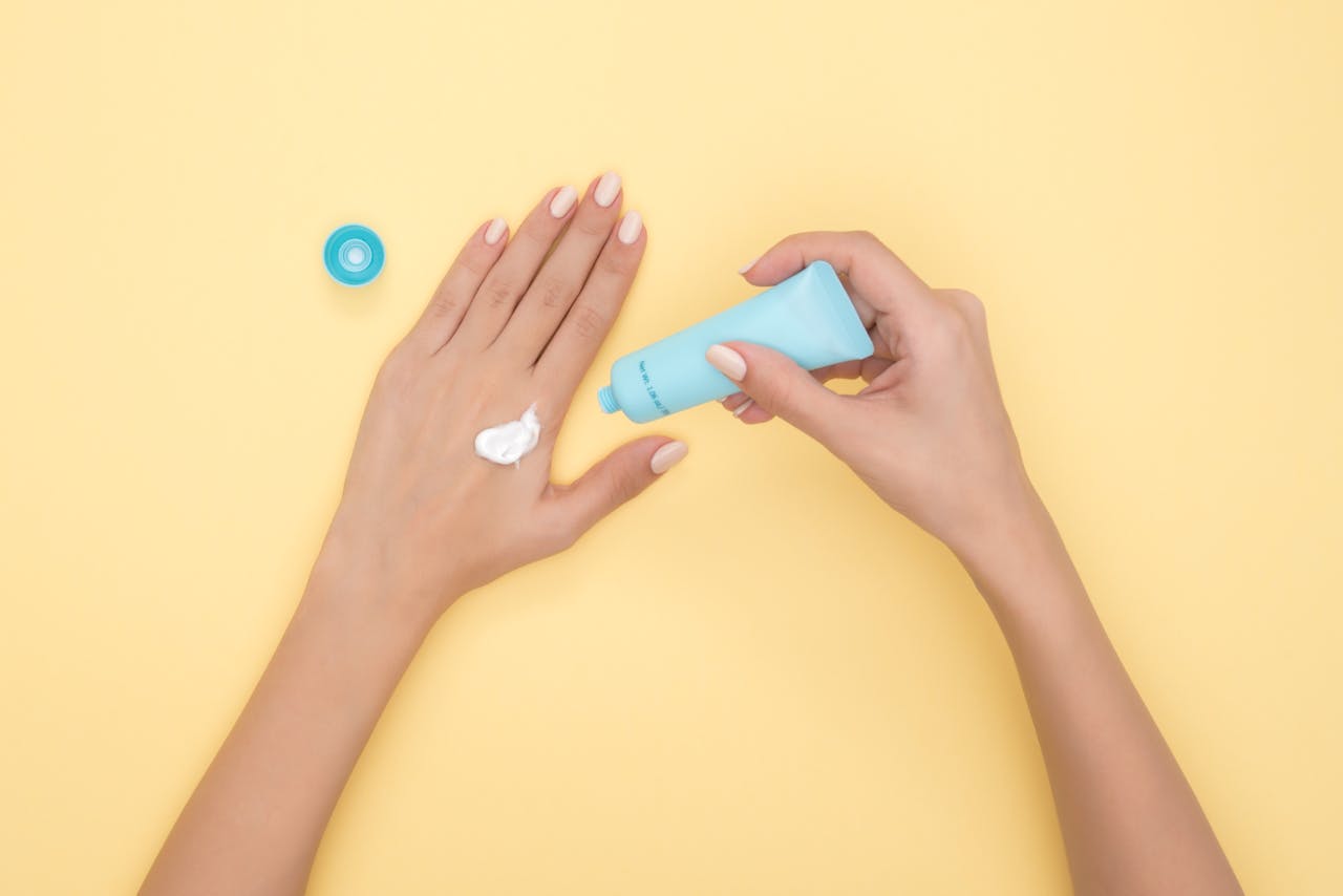 Close-up of a woman's hands applying cream on a pastel yellow background. Ideal for beauty and skincare themes.