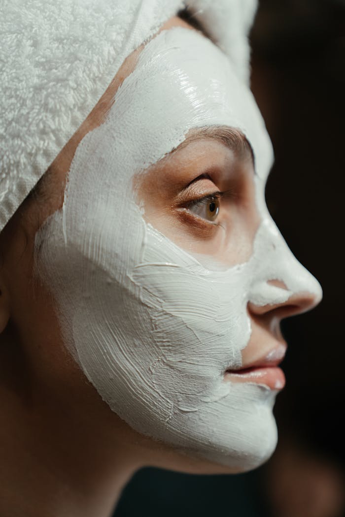 Close-up portrait of a woman with a facial mask and towel, emphasizing self-care and skincare.